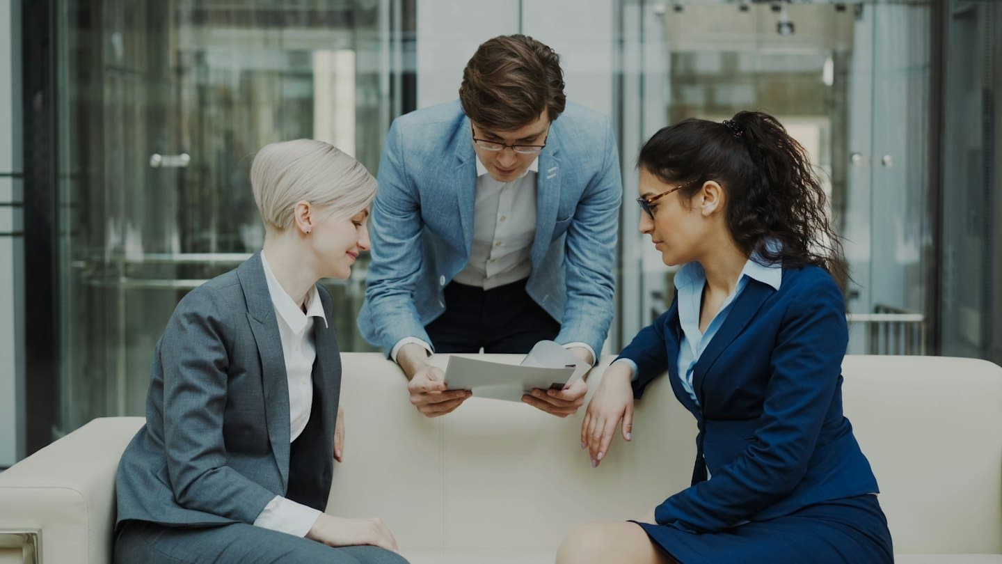 Un team di lavoro eterogeneo discute documenti su un divano in un ufficio moderno.
